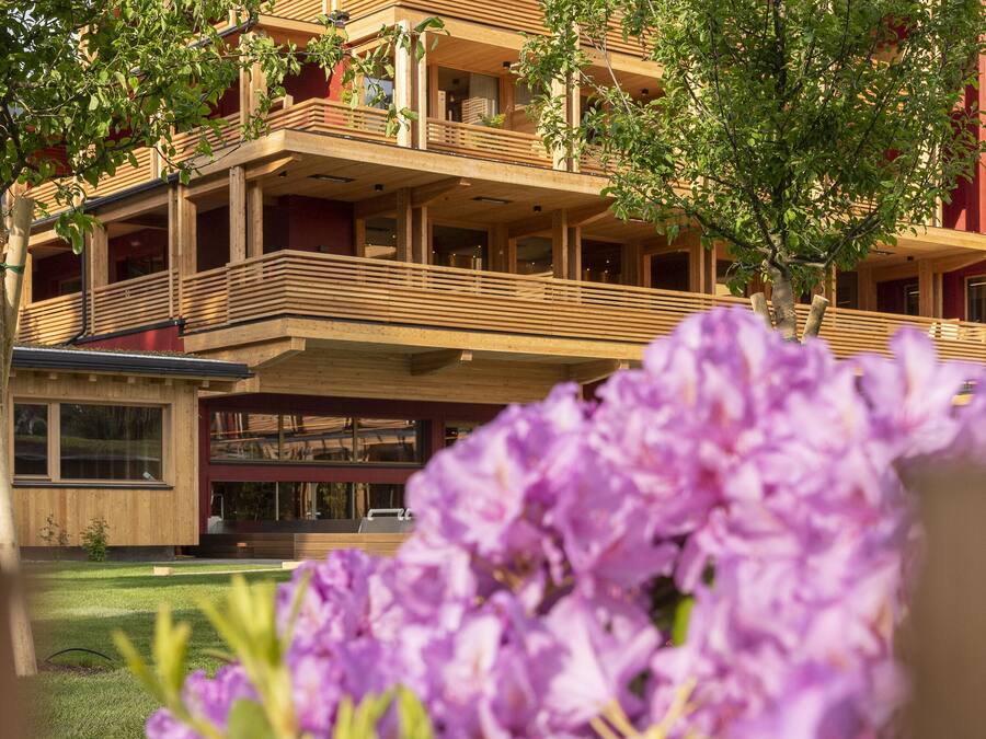 A multi-story building with balconies and a garden area with purple flowers in the foreground.
