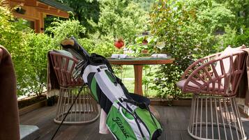 A golf bag on a wooden deck with wicker chairs, a table with a drink, and lush greenery in the background.