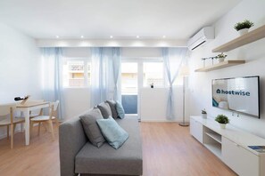 A modern living room with a sofa, a dining table, and a TV. - Cozy Bright Flats w/ Netflix | Garage by HostWise (Vila Nova de Gaia)