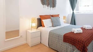Une chambre à coucher avec un lit, des tables de chevet, des plumes décoratives et une fenêtre avec des rideaux.