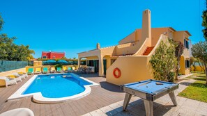 Un área de piscina con sillones de descanso, mesa de billar y un edificio con escaleras.