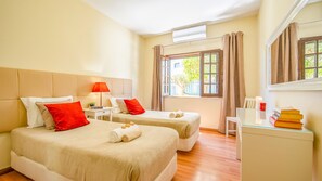 Habitación de hotel con dos camas, una mesita de noche, una lámpara, una ventana con cortinas y un escritorio con libros.