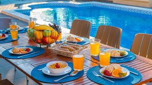 A dining table by a pool with fruit, bread, and drinks. - Villa with BBQ and heatable pool in Albufeira (Albufeira)
