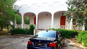 Une BMW noire était garée devant un immeuble aux colonnes blanches et à la porte rouge.