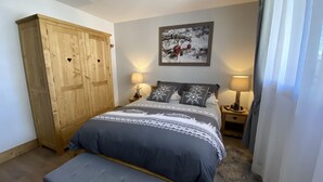 A bedroom with a large wooden wardrobe, a bed with patterned bedding, two bedside tables with lamps, and a painting on the wall. - F204 - 46 m2 -  2P+Cab - 4/6 pers (Prapoutel)