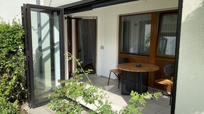 An open sliding glass door leading to a patio area with a round wooden table and two chairs, a small potted plant, and a view of the outside. - Ferienwohnung mit Terrasse (Metzingen)