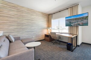 A hotel room with a large window, a flat-screen TV, a sofa, a desk, and a chair.