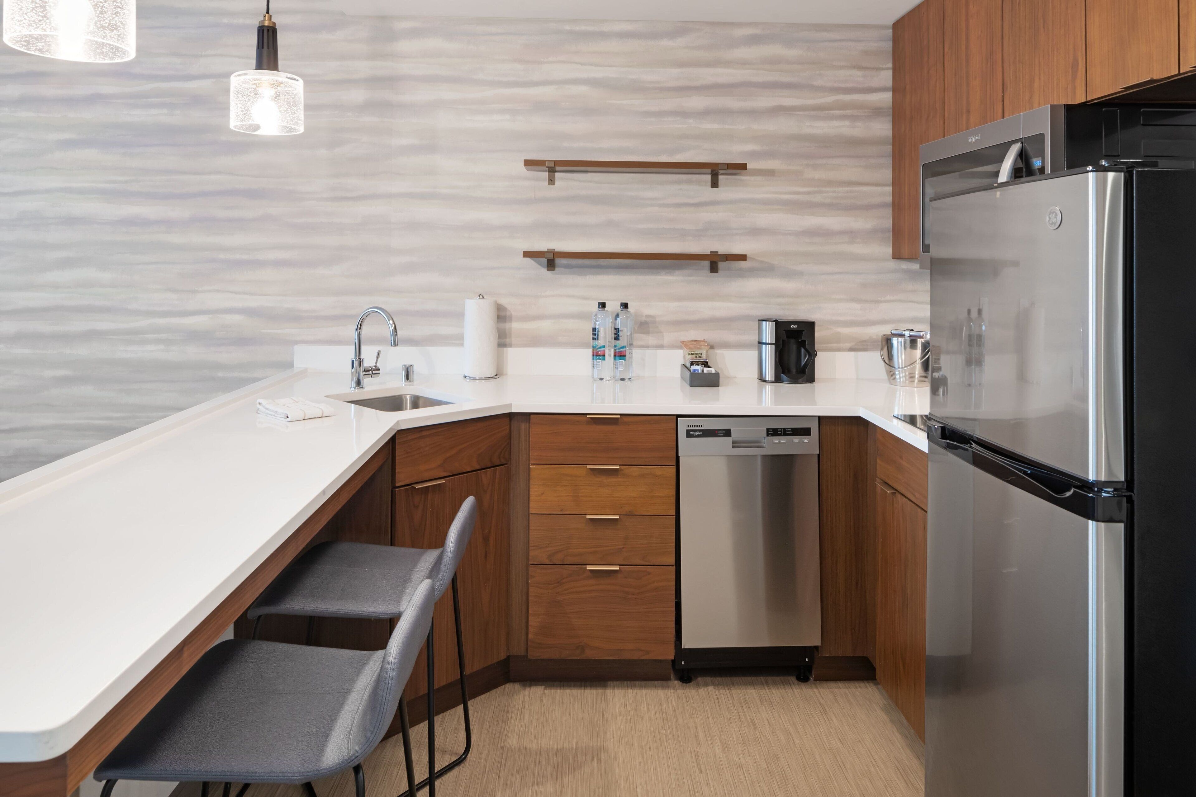 A modern kitchen with a white countertop, wooden cabinets, a stainless steel refrigerator, and a dishwasher.