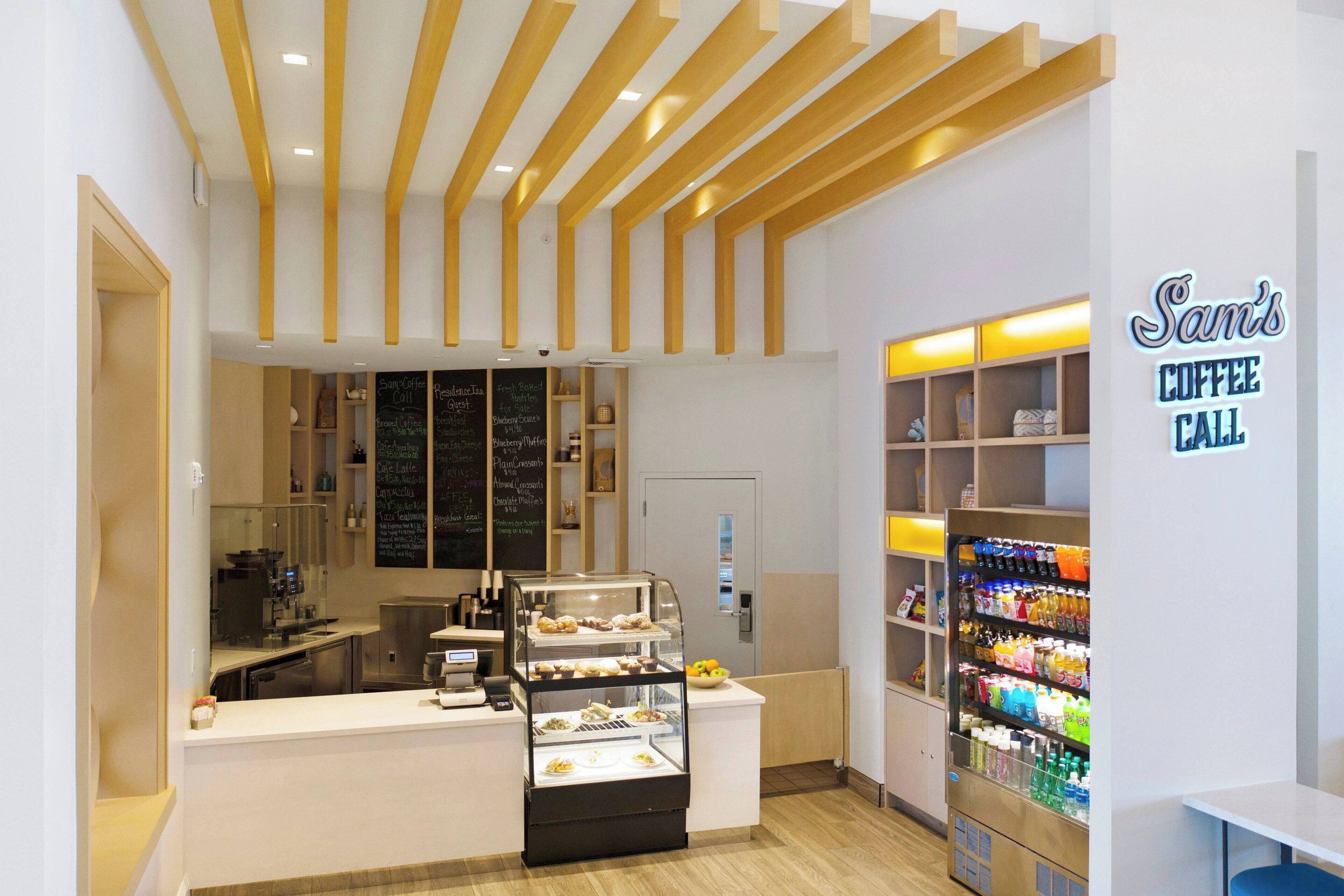 A coffee shop interior with a counter, a display case with pastries, a beverage vending machine, and a chalkboard menu.