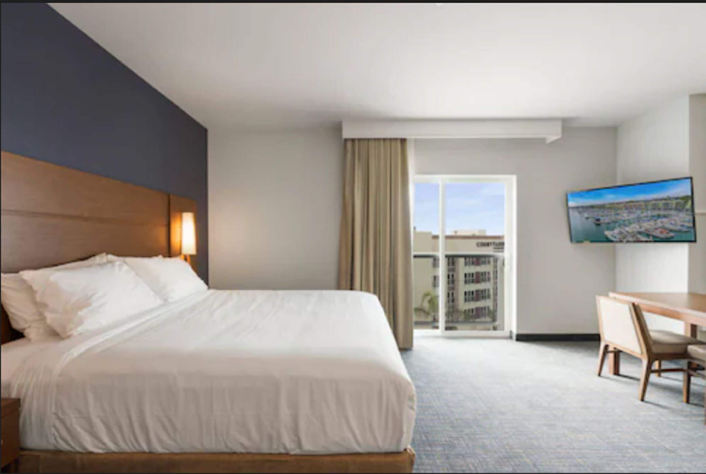 Ein Hotelzimmer mit einem großen Bett, einem Schreibtisch, einem Sessel, einem Fernseher und Blick auf die Stadt.