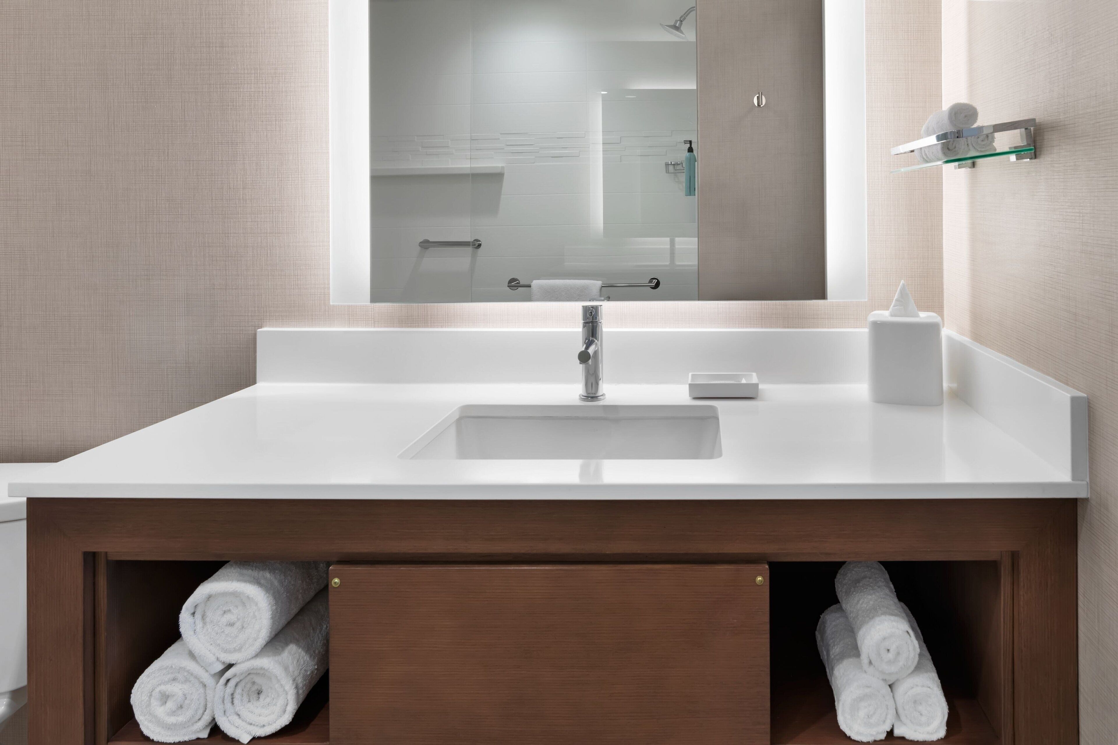A modern bathroom with a white sink, a mirror, and wooden cabinets below.