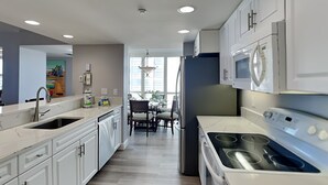 A modern kitchen with white cabinetry, a stainless steel sink, a built-in oven, and a microwave. - Gullwing 606 by Distinctive Beach Rentals (Fort Myers Beach)