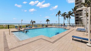 A swimming pool with a view of the ocean, surrounded by palm trees and lounge chairs. - Gullwing 606 by Distinctive Beach Rentals (Fort Myers Beach)