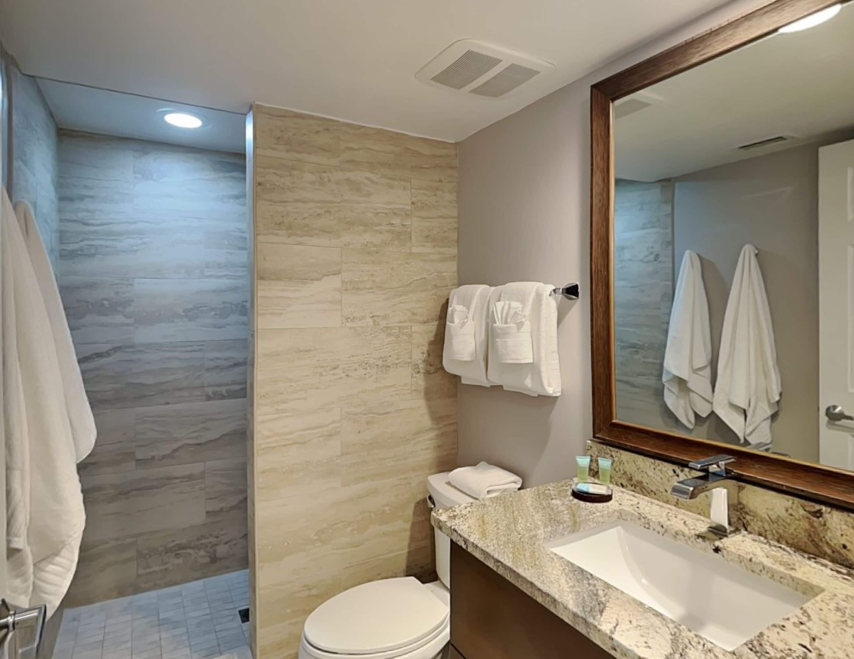 A modern bathroom with a marble countertop, a large mirror, and a toilet.