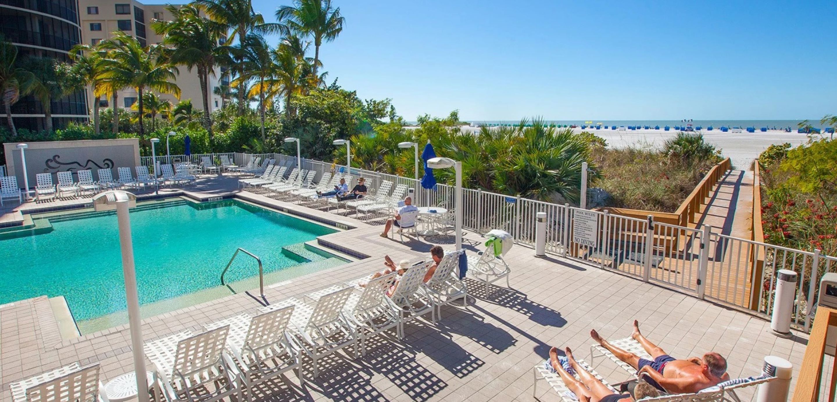 A pool area with lounge chairs and a view of the beach.