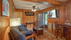 A cozy cabin interior with a sofa, coffee table, dining table, and a view of deer outside.