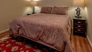 A bedroom with a large bed, two bedside tables with lamps, a nightstand, and a red patterned rug.