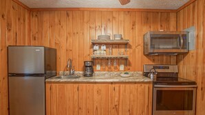 A compact kitchen with wooden paneling, a stainless steel refrigerator, a coffee maker, a microwave, and an oven.