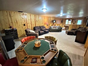 A room with a wooden paneled wall, a green octagonal table with chairs, a sofa, and a television. - Diamond Jewel - Pool table, Fire Pit (Deadwood)