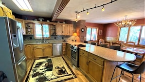 A kitchen with wooden cabinets, a refrigerator, an oven, a dishwasher, a dining area with a table and chairs, and a chandelier. - Diamond Jewel - Pool table, Fire Pit (Deadwood)