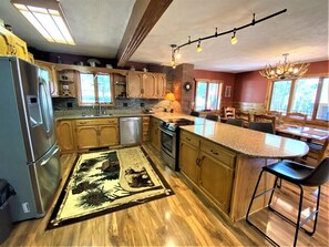 A kitchen with wooden cabinets, a refrigerator, an oven, a dishwasher, a dining area with a table and chairs, and a chandelier. - Diamond Jewel - Pool table, Fire Pit (Deadwood)