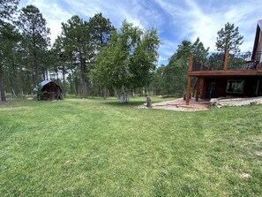 A grassy yard with a wooden cabin and a modern house with a balcony. - Diamond Jewel - Pool table, Fire Pit (Deadwood)