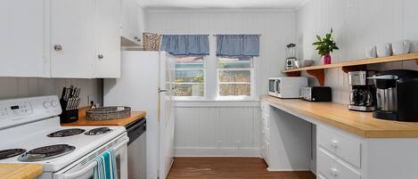 Een kleine keuken met witte keukenkastjes, een fornuis, een magnetron en een koffiezetapparaat.