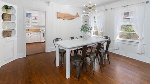 Un comedor con una mesa y sillas blancas, techo de madera y vista al jardín a través de una ventana.