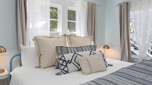 Un dormitorio con cama, almohadas, mesita de noche y cortinas.