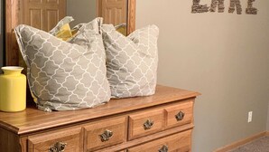 Un aparador de madera con almohadones estampados y un jarrón amarillo.
