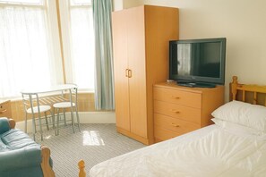 A hotel room with a bed, a television on a wooden cabinet, a small table with chairs, and a window with curtains.