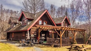 A log cabin with a wooden porch and picnic table, surrounded by trees.