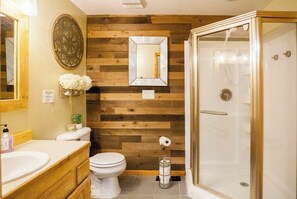 A bathroom with a wooden wall panel, a toilet, a sink, a mirror, and a glass-enclosed shower.
