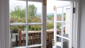 A room with a large window offering a view of a garden and a wooden deck. - Church Cottage (Bridport)