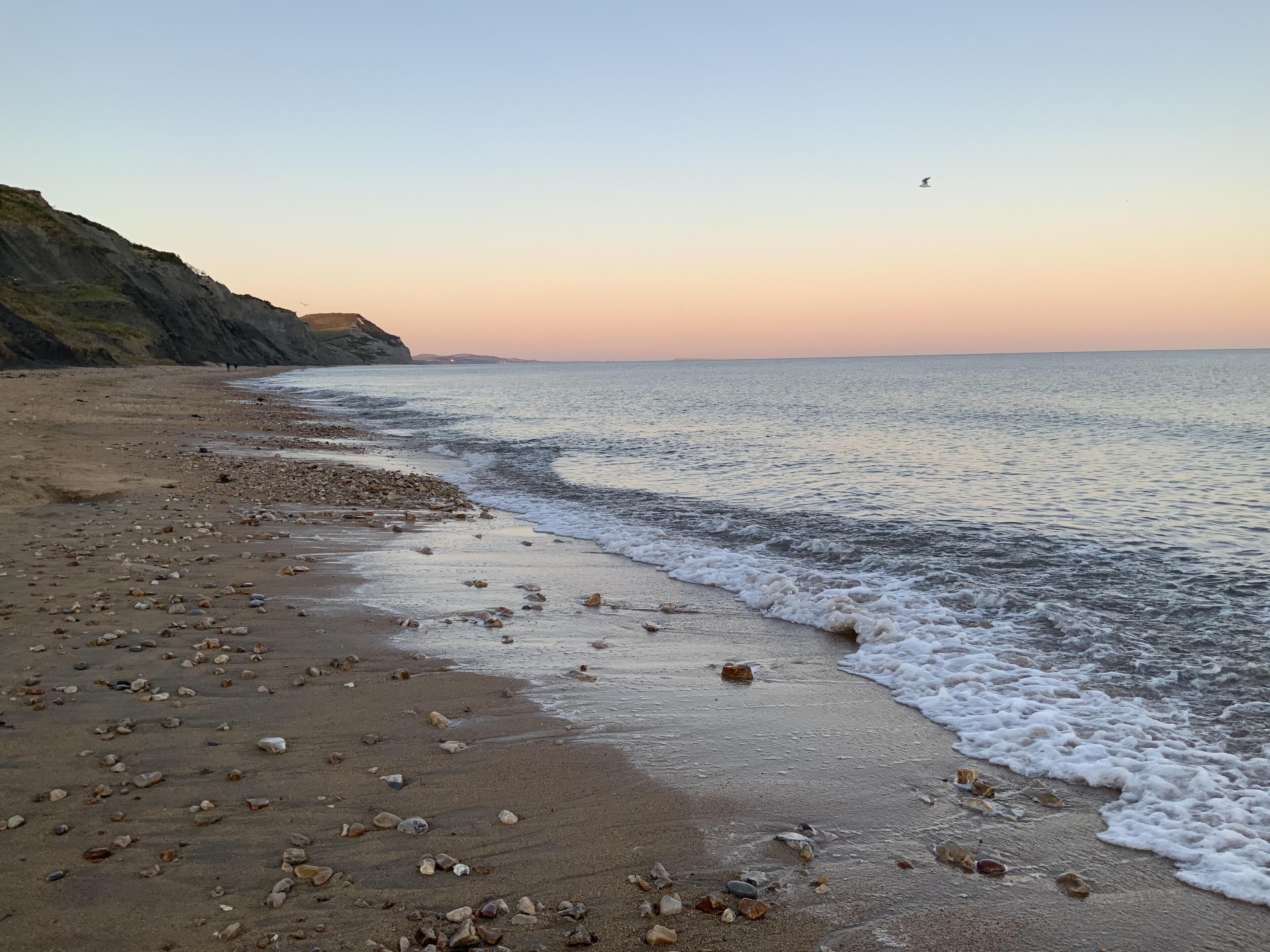 A beach with pebbles and a calm sea.