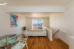 A modern living room with a glass table, white sofa, and a colorful abstract painting.