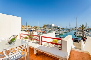 A balcony with a view of a marina, a glass table, and a chair.