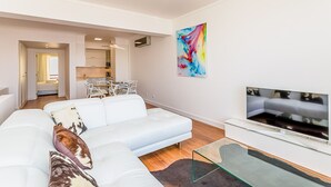 En moderne stue med en hvid sofa, et glasbord og et fladskærms-tv.