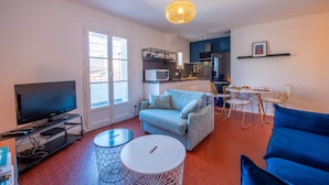 Un salon moderne doté d’un téléviseur à écran plat, d’un canapé bleu clair, d’une table ronde blanche et d’un coin repas avec des chaises et une petite table.