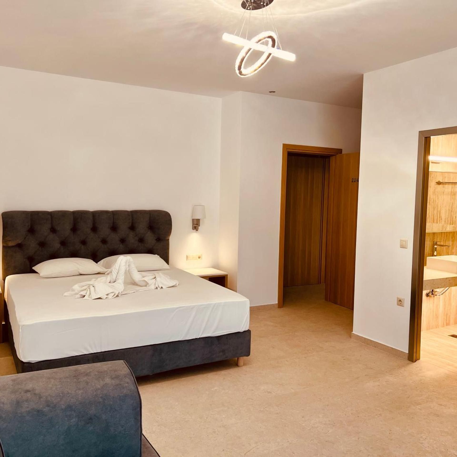 A modern bedroom with a large bed, bedside tables, a wardrobe, and a bathroom visible through an open door.