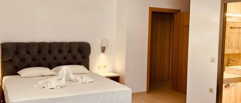 A modern bedroom with a large bed, bedside tables, a wardrobe, and a bathroom visible through an open door.