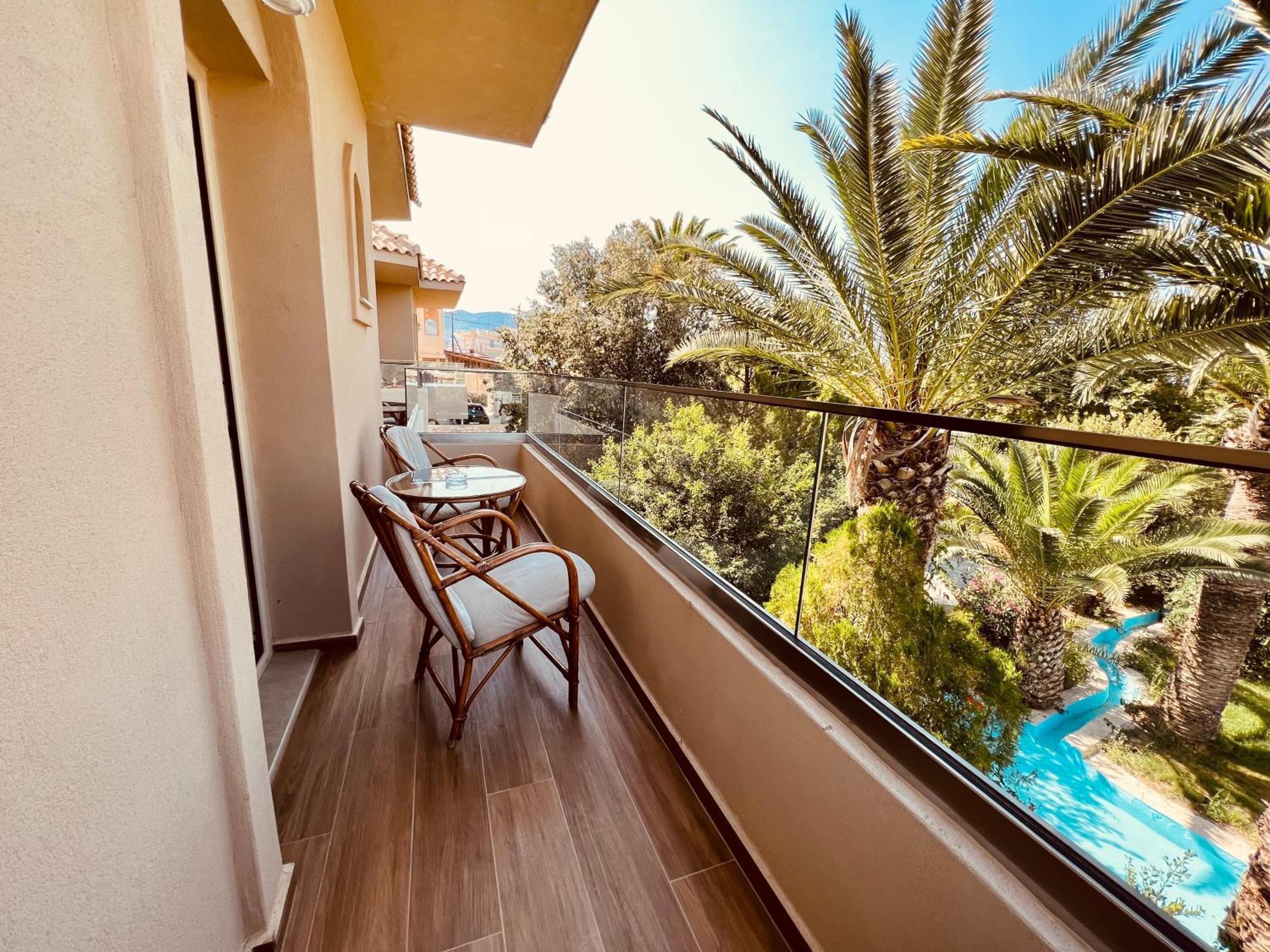A balcony with a table and chairs, overlooking a pool and lush greenery.