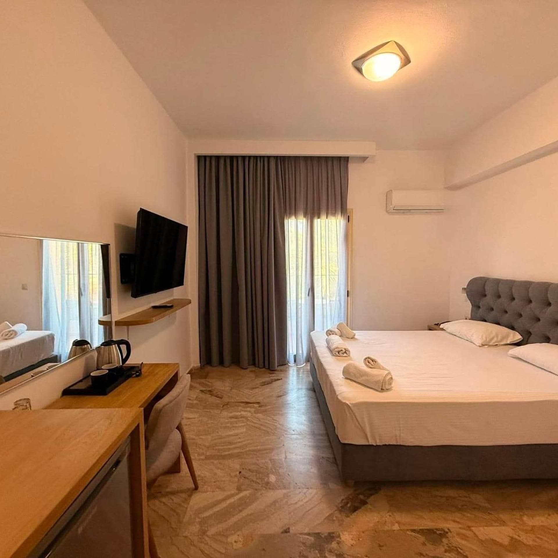 A hotel room with a bed, a desk with a television, a coffee maker, and a window with curtains.