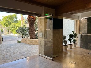 A reception area with a glass door, stone flooring, and potted plants. - Lili Hotel (Malevizi)