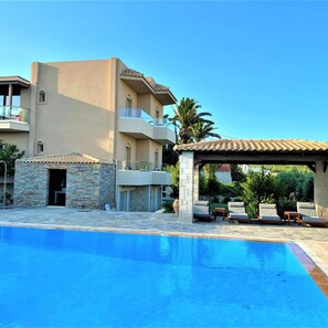 A modern hotel with a swimming pool, outdoor seating, and a stone facade. - Lili Hotel (Malevizi)