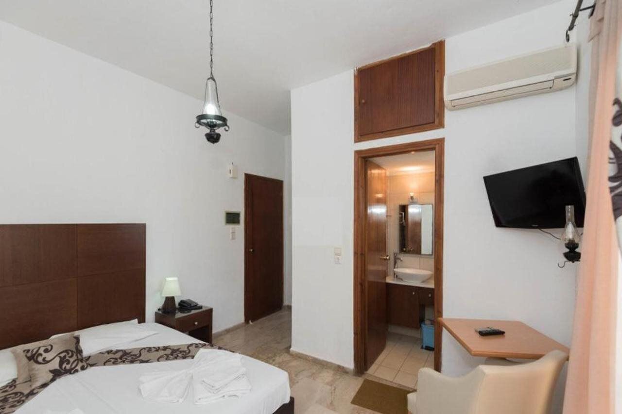 A hotel room with a bed, bedside table, lamp, TV, and a small desk with a chair.