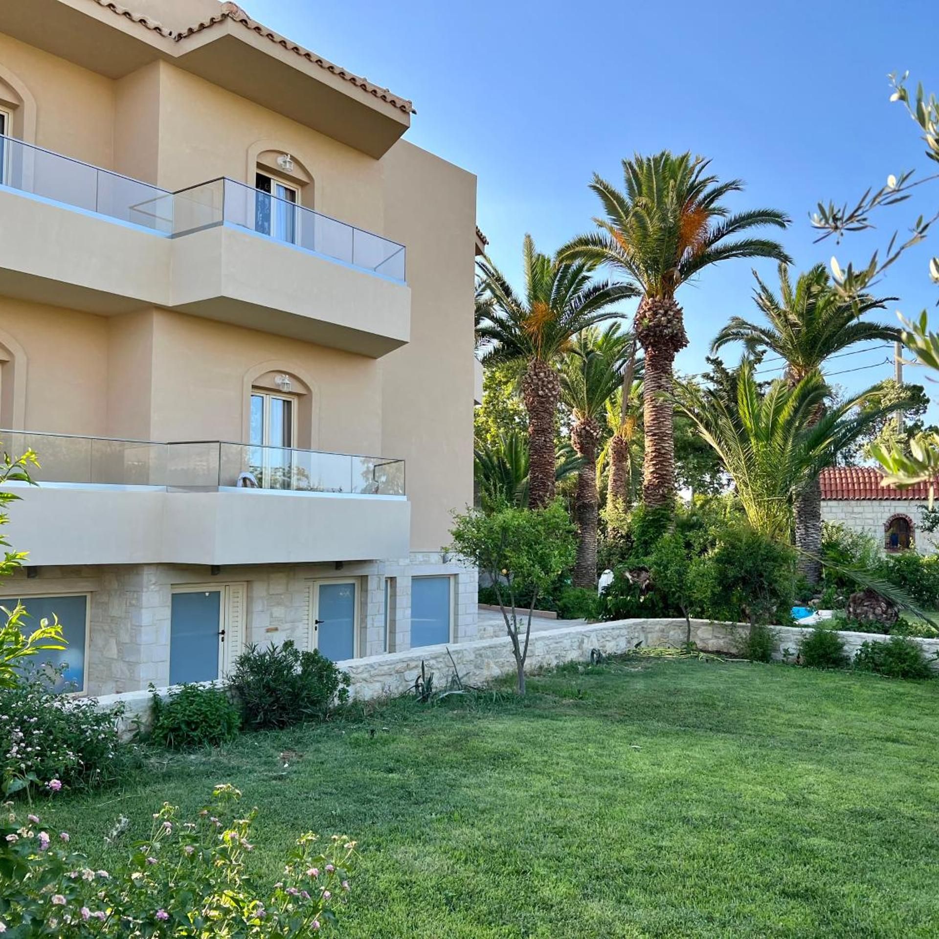 A multi-story building with balconies, a well-maintained lawn, and palm trees.
