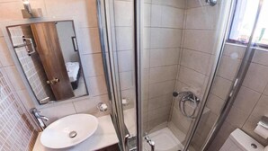 A modern bathroom with a glass-enclosed shower, a sink with a mirror, and a toilet. - Lili Hotel (Malevizi)