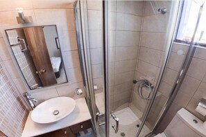 A modern bathroom with a glass-enclosed shower, a sink with a mirror, and a toilet. - Lili Hotel (Malevizi)