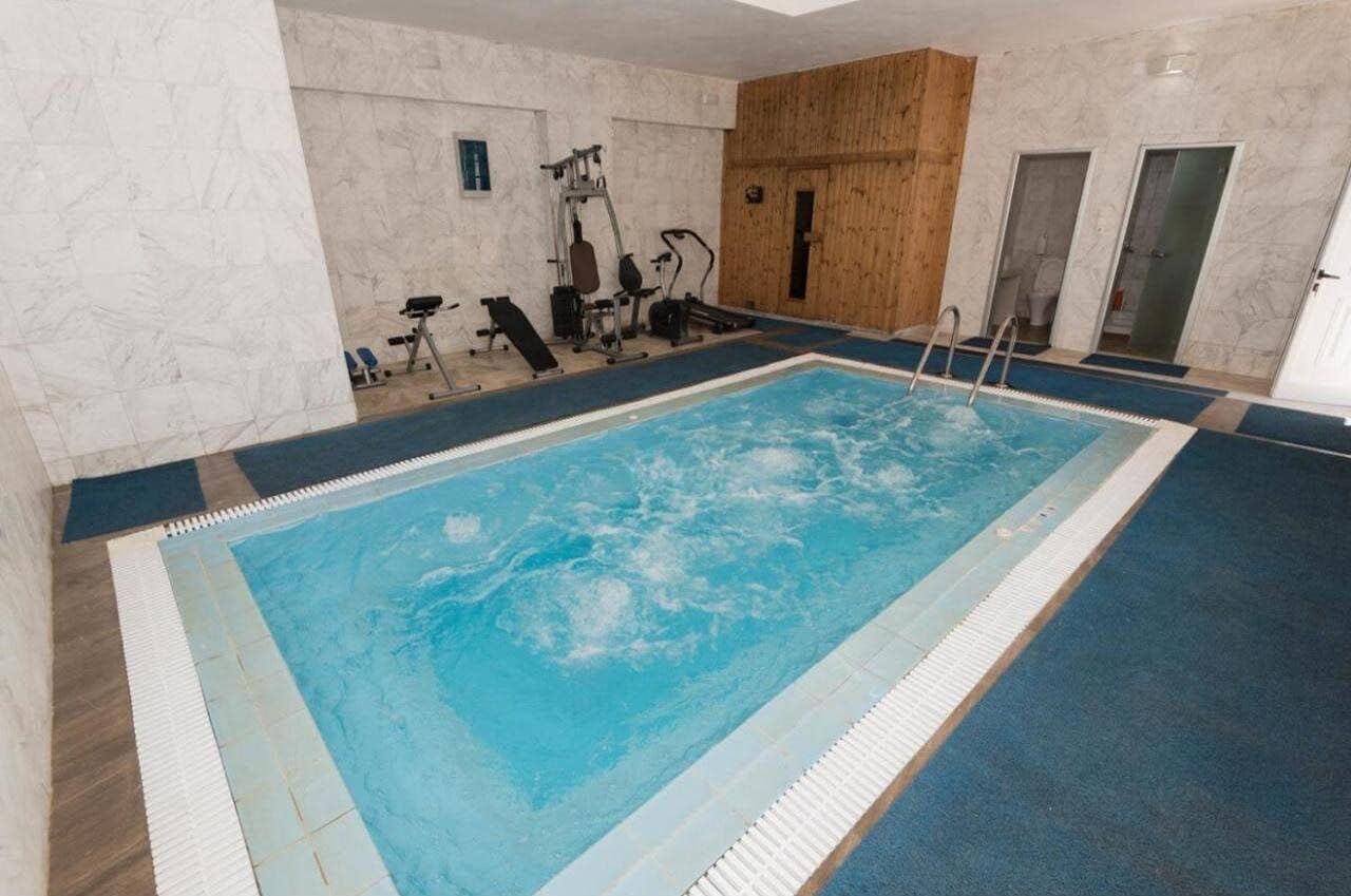 An indoor swimming pool with exercise equipment and a wooden wall.